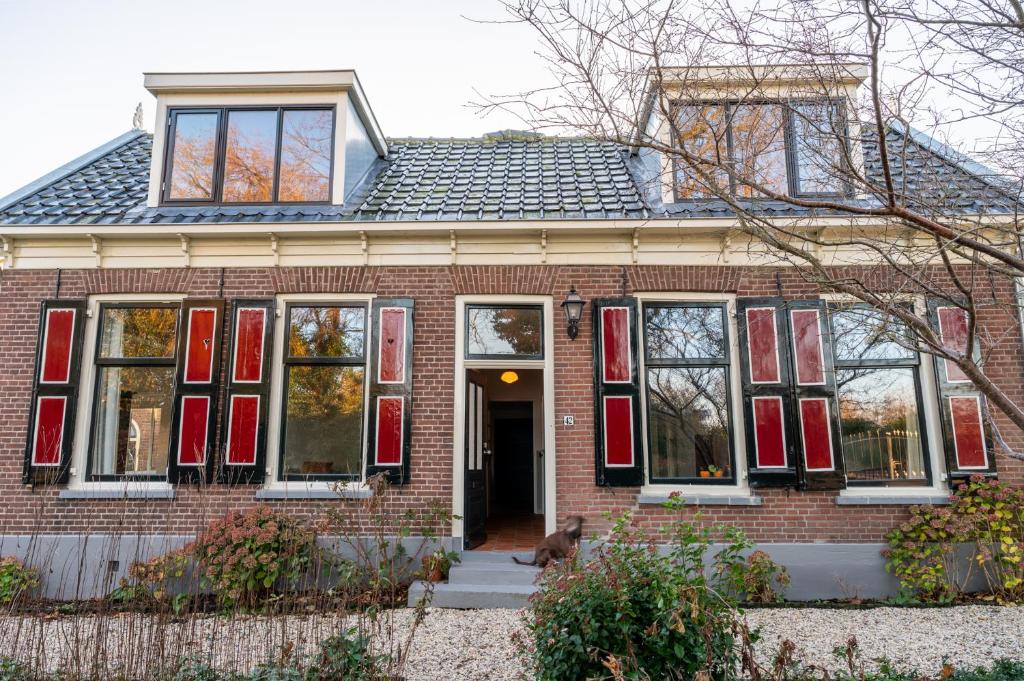 una casa de ladrillo rojo con un perro sentado frente a ella en Kleinhoef - charmante, luxe kamers in een boerderij uit 1875, en Nigtevecht