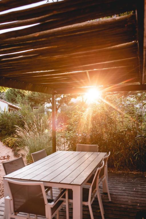 a wooden table and chairs on a patio with the sun at Le Phare in Les Portes