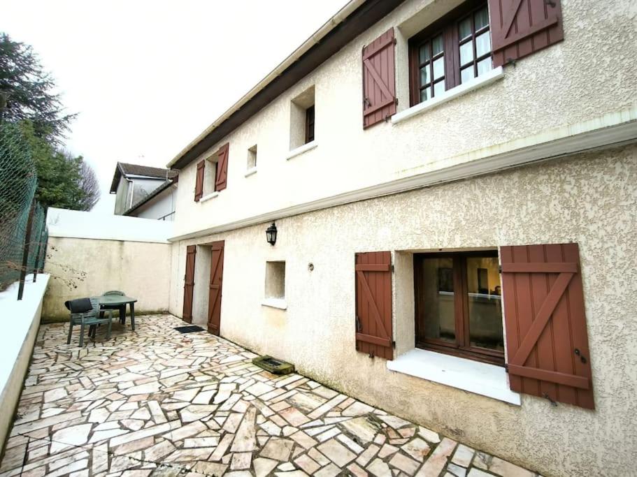 a building with brown doors and a stone patio at Maison RNA spacieuse 5 chambres in Saint-Witz