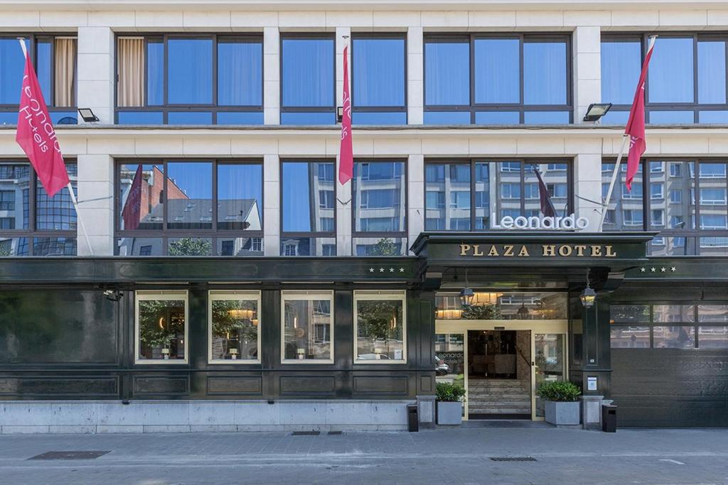 Um edifício com duas bandeiras cor-de-rosa à frente. em Leonardo Hotel Antwerp The Plaza em Antuérpia