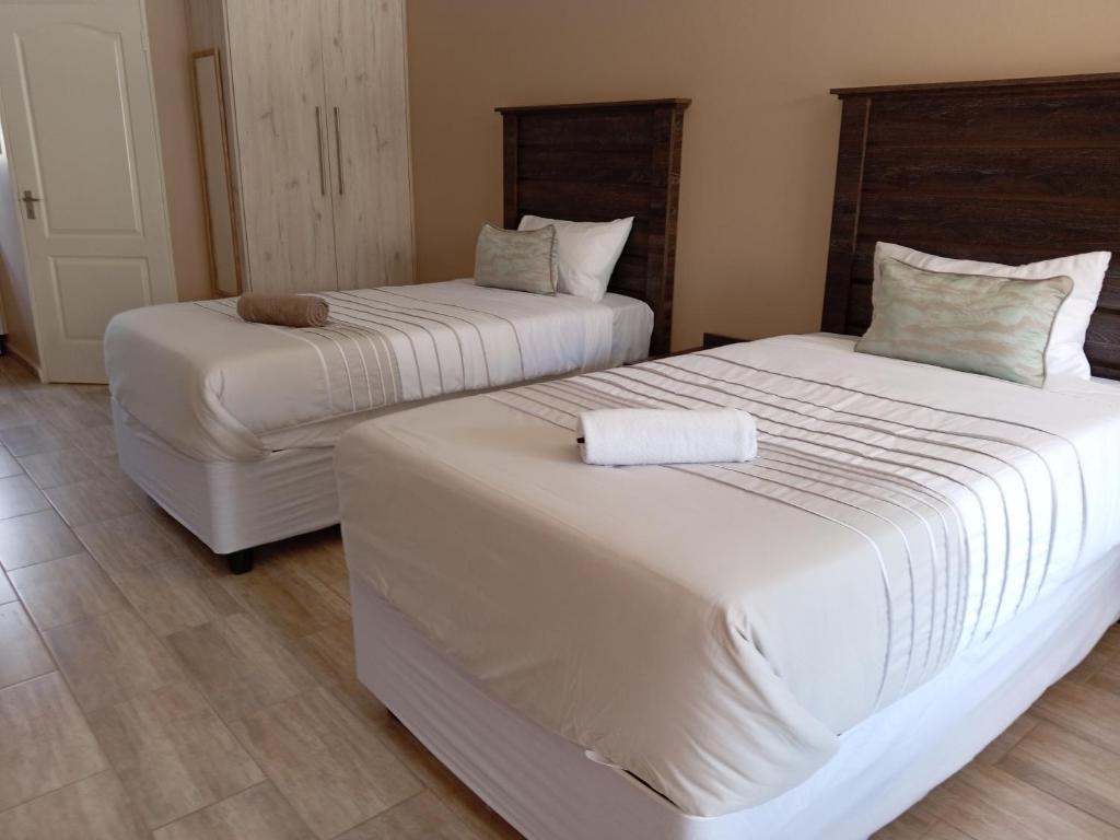 two beds in a hotel room with white sheets at AMANI PALMS GUEST HOUSE in Klerksdorp