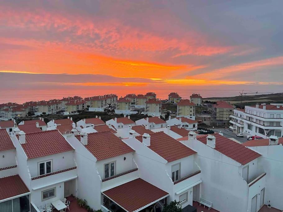 Ericeira Beach Apartment في إيريسييرا: مجموعة من البيوت البيضاء ذات السطوح الحمراء تحت غروب الشمس
