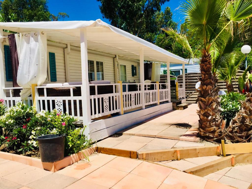 une maison blanche avec une véranda et des palmiers dans l'établissement MOBIL HOME PLAGE DE PAMPELONNE SUR UN TRES BEL EMPLACEMENT SURPLOMBANT LA BAIE DE PAMPELONNE, à Saint-Tropez