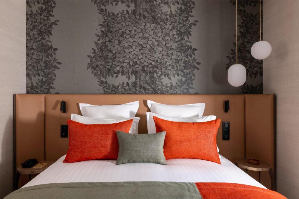 a bedroom with a bed with orange and grey pillows at Hôtel L'Ormaie & Spa in Paris