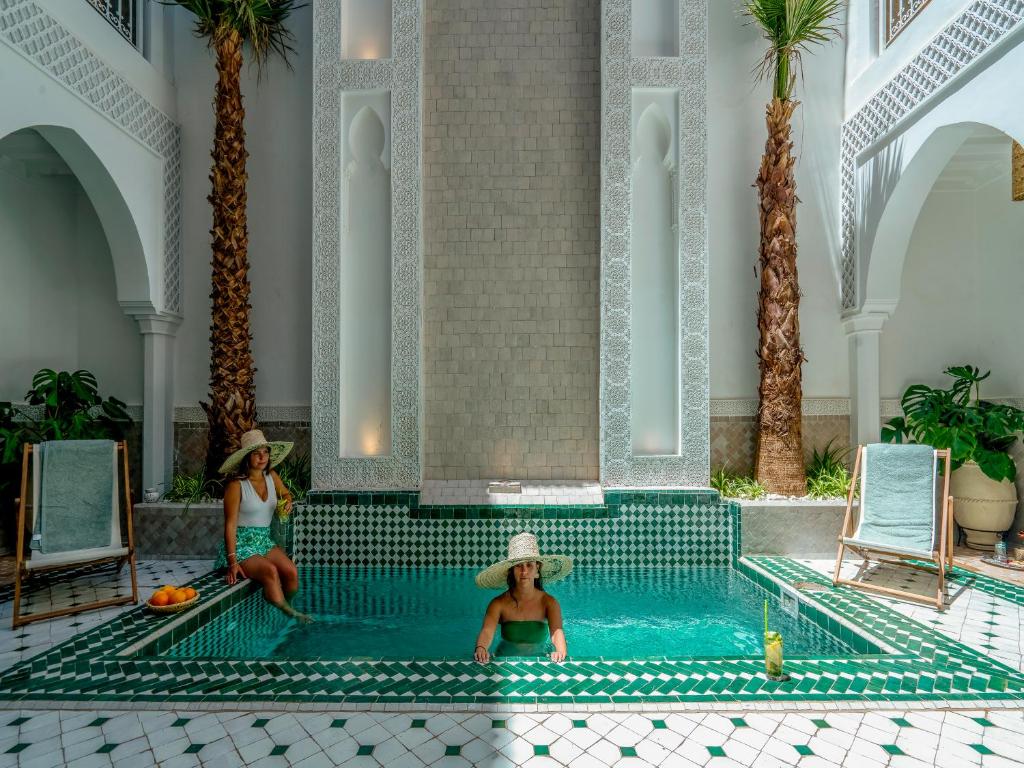 Dos mujeres sentadas en una piscina en un complejo en Riad Nelia De Marrakech Hotel Boutique & Spa, en Marrakech