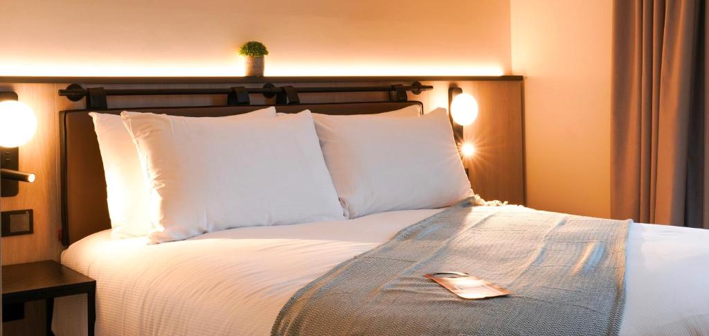 1 cama con almohadas blancas y control remoto. en Southgate Hotel London en East Barnet