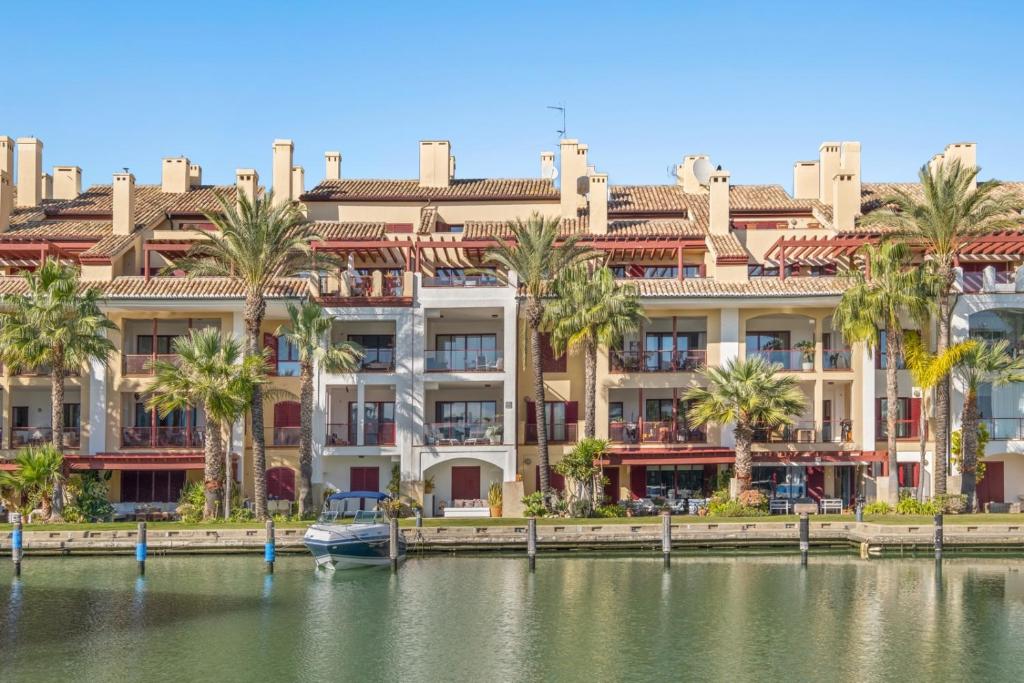 a large building with palm trees in front of a body of water at Palm Serenity - Sotogrande in Sotogrande