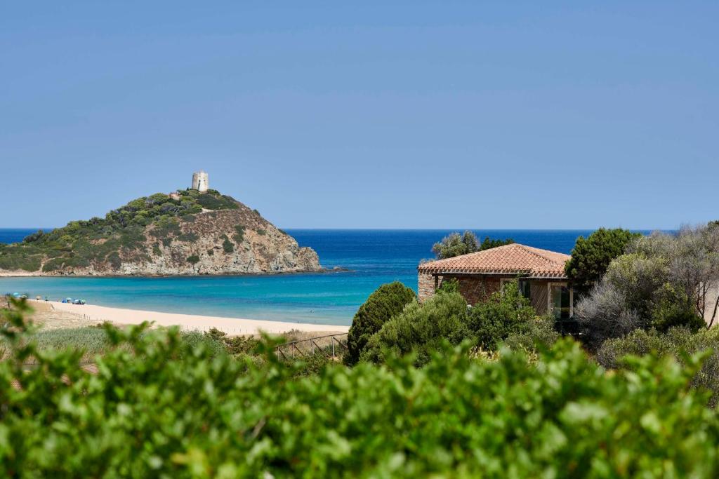 a beach with a house and the ocean w obiekcie Baia Di Chia Resort Sardinia, Curio Collection By Hilton w mieście Chia