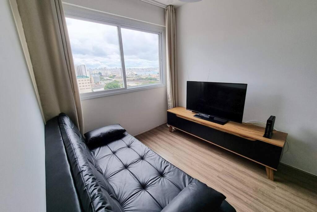 a living room with a couch and a large window at Ap10 Prático, confortável com wifi, piscina, rooftoop e academia em frente ao Metrô in Sao Paulo