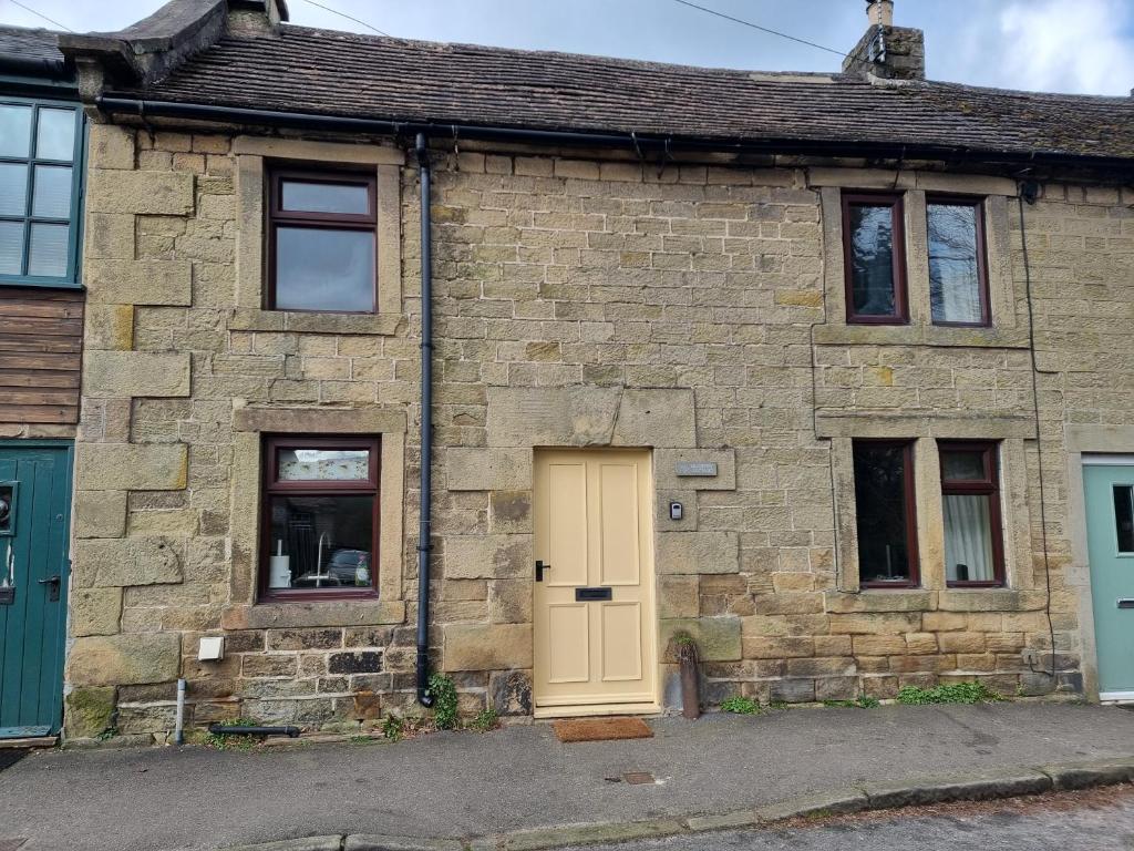 a brick house with a yellow door and windows at Mulberry Cottage in Bakewell