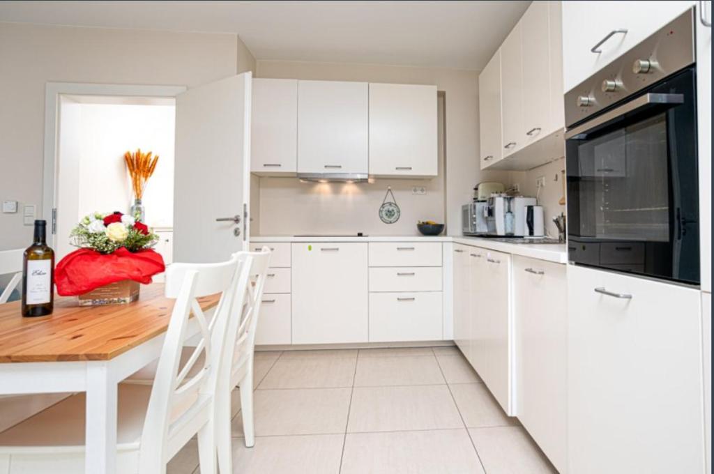 a white kitchen with white cabinets and a wooden table at Elegant Spacious Room with Open Kitchen, Steps from Luxembourg Train Station in Luxembourg