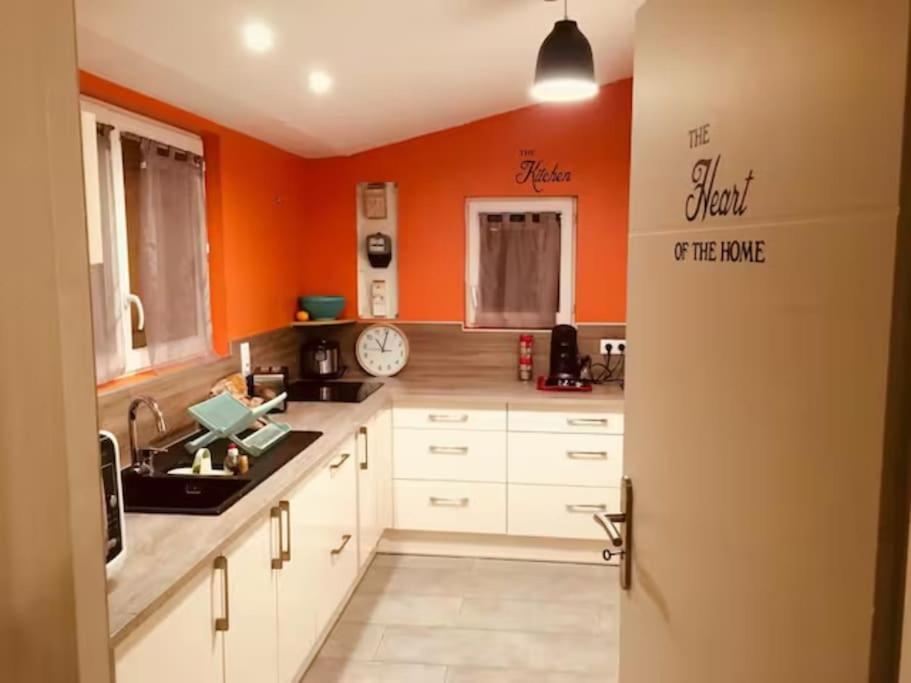 - une cuisine avec des murs orange et des armoires blanches dans l'établissement Maison Téranga 2 Chambres Et 2 mezzanines et 2 parking gratuits, à Courrejean