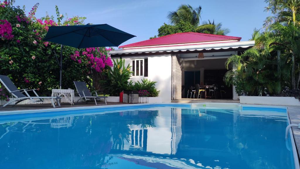 a swimming pool with an umbrella next to a house at Les Coulirooms - Gîte in Sainte-Anne