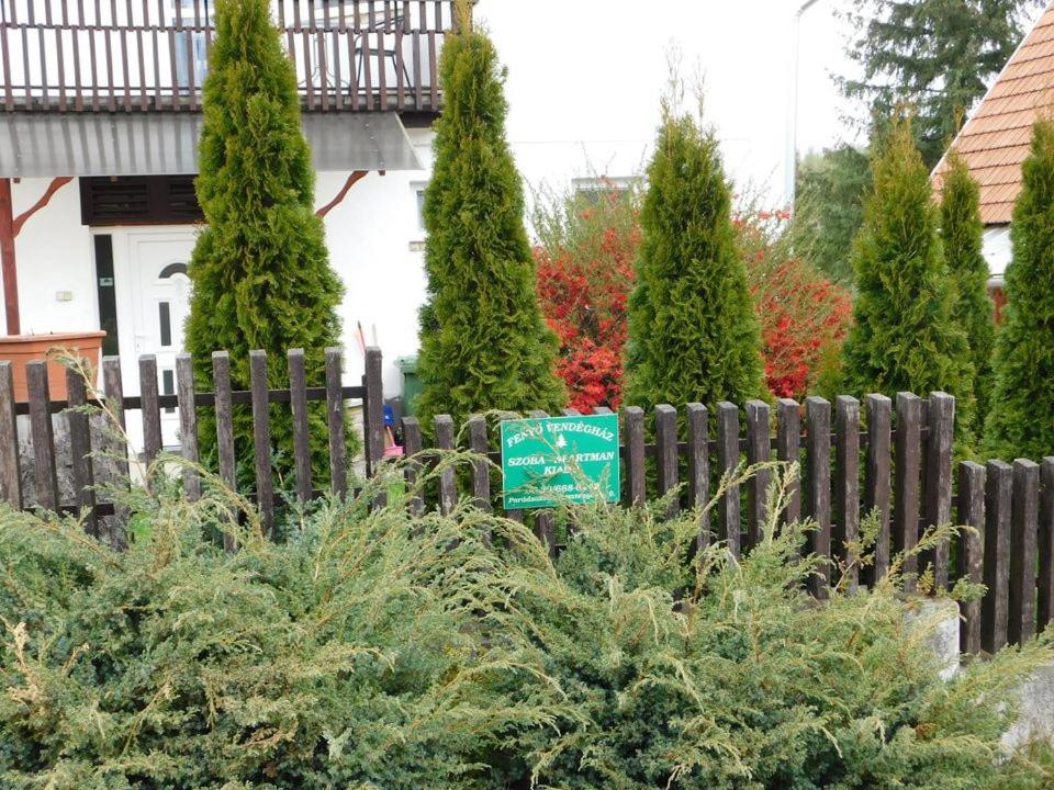 a fence with trees in front of a house at Fenyő Vendégház in Parádsasvár