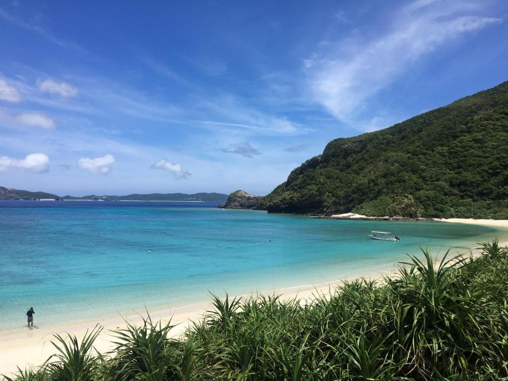 a person walking on a beach with blue water at HOTEL KANALOA in Tokashiki