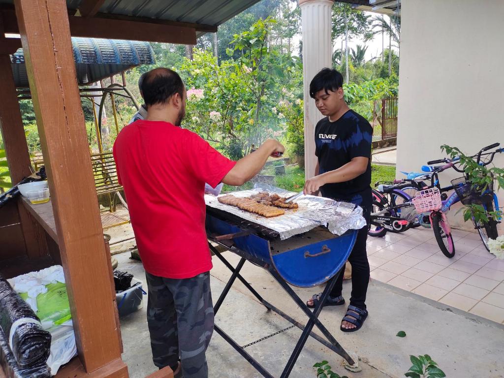two men preparing food on a barbecue grill at hotel lake town resort. in Kuala Kangsar