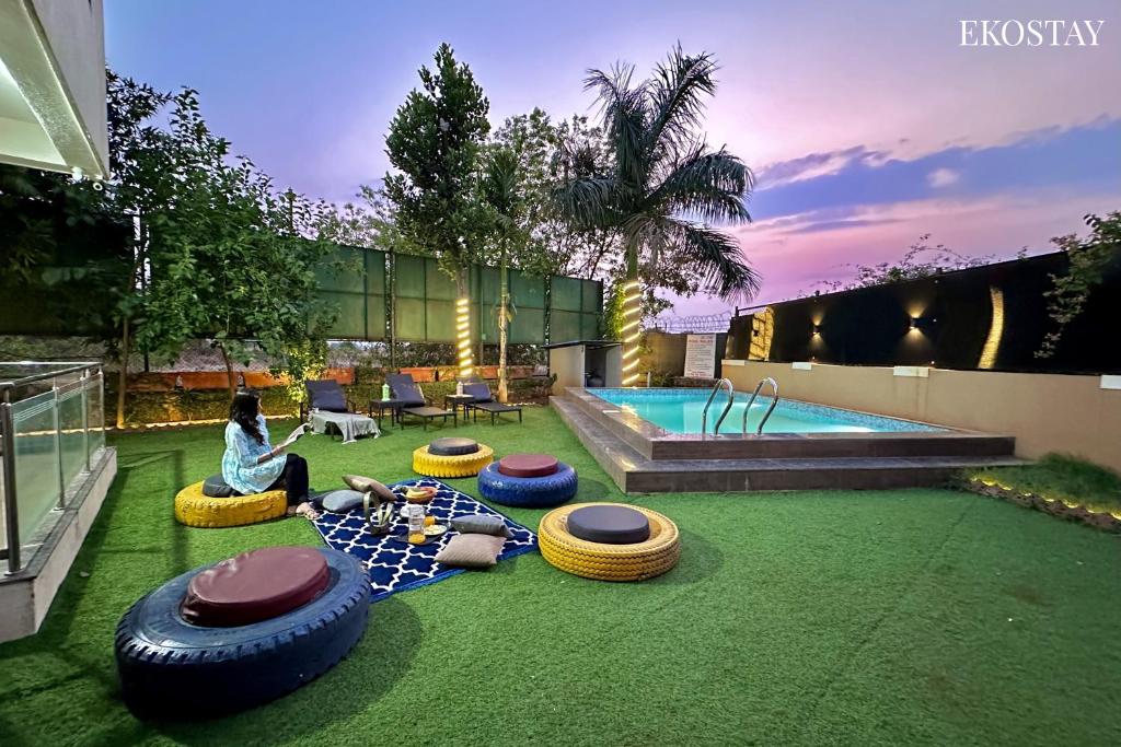 a woman sitting on the grass next to a pool with tires at EKOSTAY Gold - Iris Villa in Lonavala