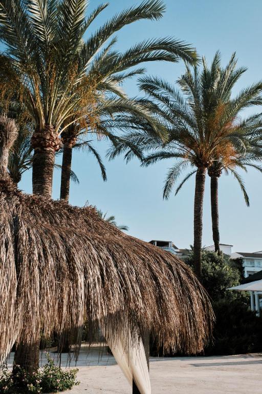 two palm trees with a straw roof on a beach at Prinsotel La Dorada & Spa in Playa de Muro