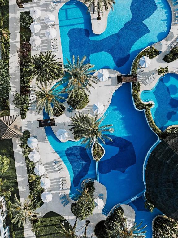 an aerial view of a resort swimming pool with palm trees at Prinsotel La Dorada & Spa in Playa de Muro