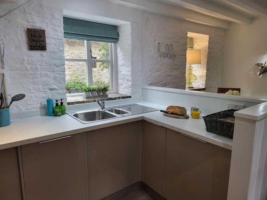 a white kitchen with a sink and a window at Guest Homes - Clara Cottage in Bretforton