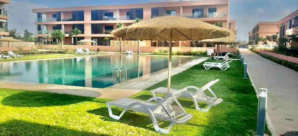 2 ligstoelen en een parasol naast een zwembad bij Belle vue, noria golf in Marrakesh
