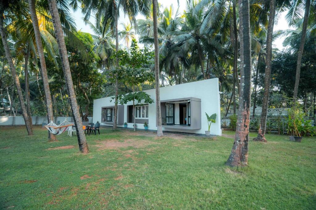 una casa blanca con palmeras delante en Cabana by GRHA - Charming Cottage at Kappad Beach, en Kozhikode