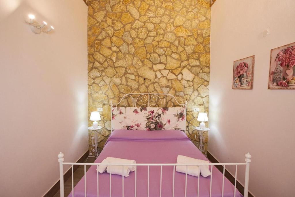ein Schlafzimmer mit einem lila Bett und einer Steinmauer in der Unterkunft La casa di Marilù in Marsala