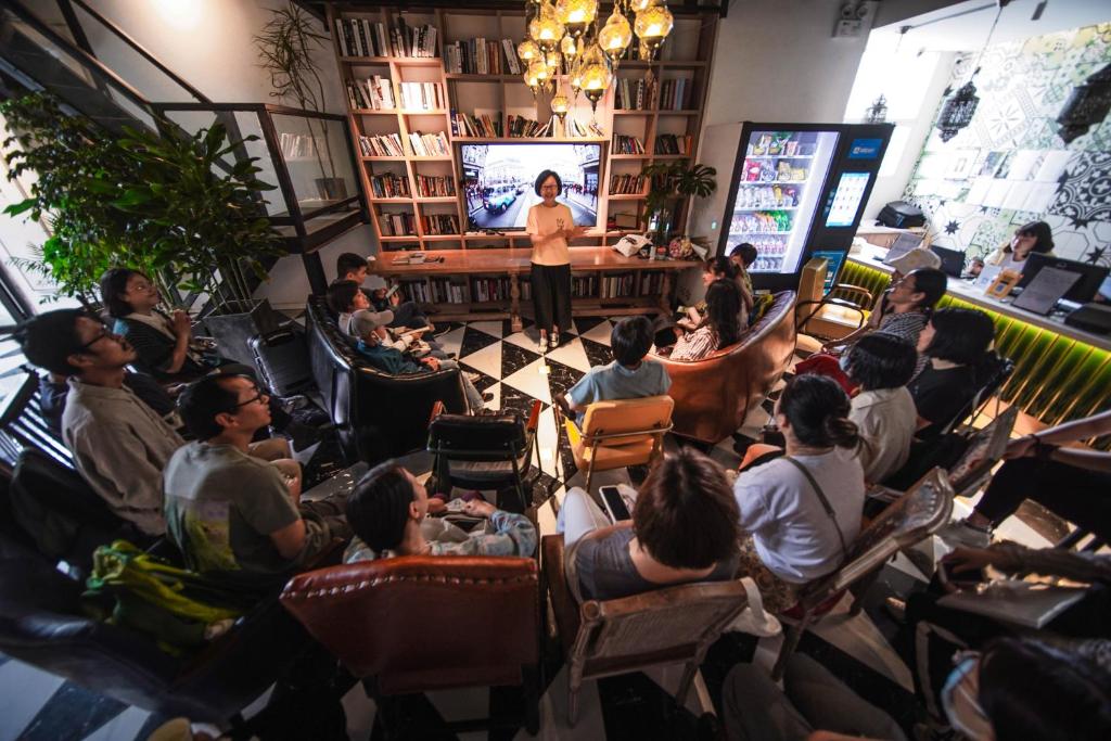 POSHPACKER·Chengdu Local Tea Hostel في تشنغدو: مجموعة من الناس يجلسون في غرفة يشاهدون العرض التقديمي