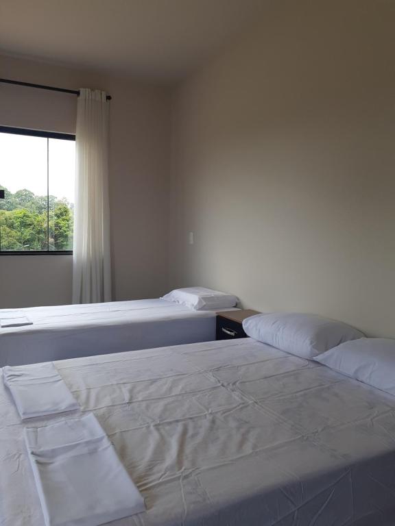 2 Betten in einem weißen Zimmer mit Fenster in der Unterkunft Suítes Flor do Maracujá 01 in Ponta Grossa