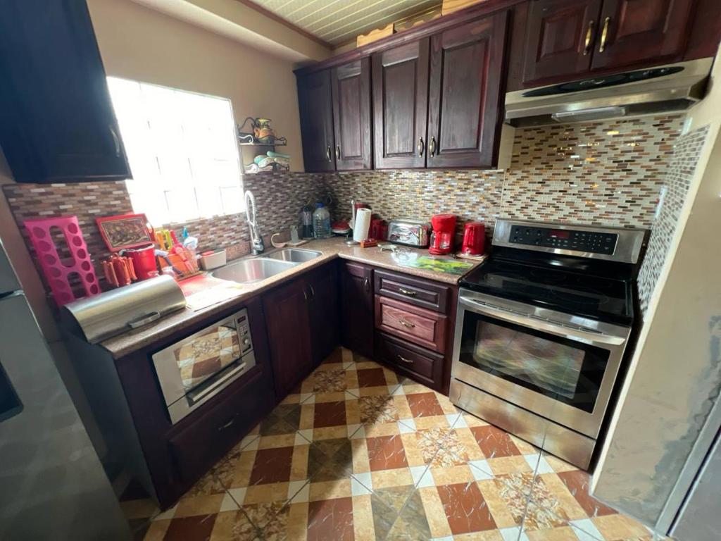 cocina con armarios de madera y suelo de baldosa en NEXXUS, en Trincity 