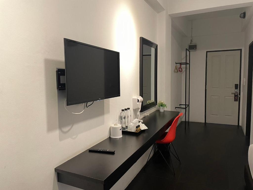 A room work area with a long black desk, red chair, television and entry door.