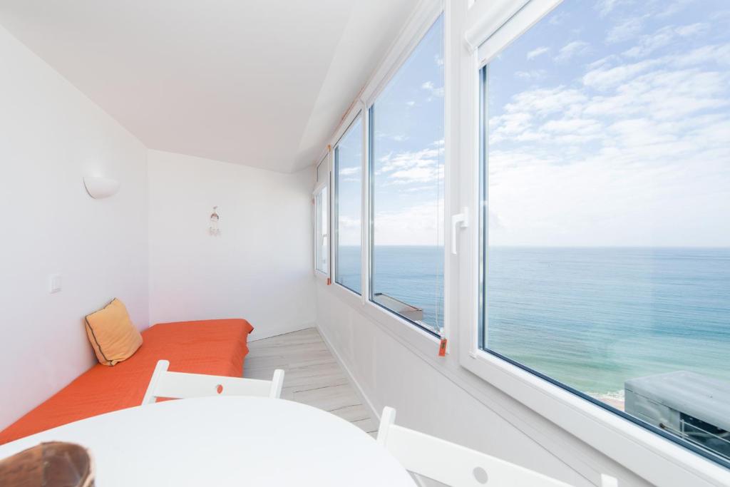 Cette chambre blanche dispose d'une grande fenêtre donnant sur l'océan. dans l'établissement Apartamento Sol da Falésia, à Sesimbra