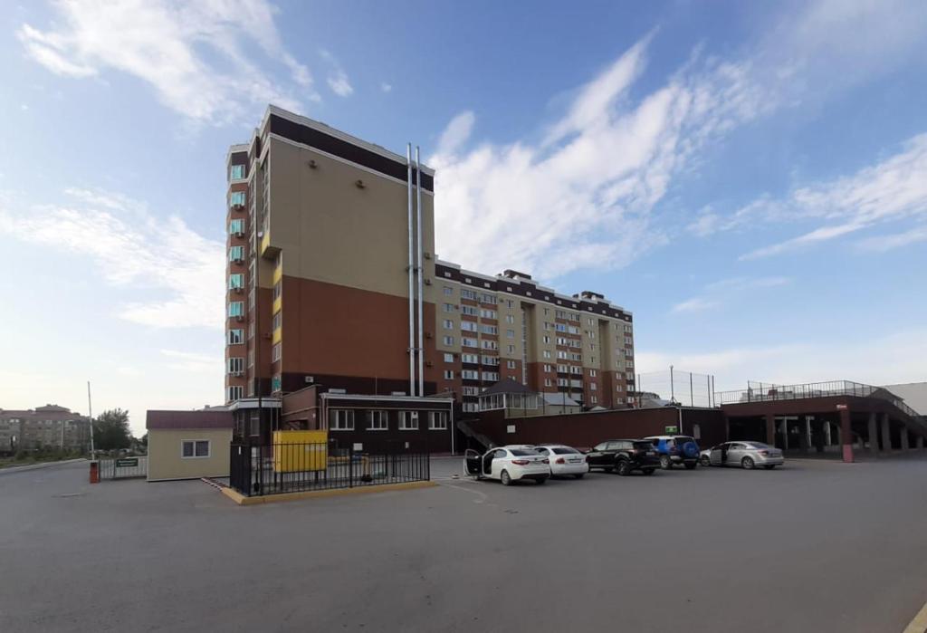 un gran edificio con coches estacionados en un estacionamiento en Абажур, en Aktobe