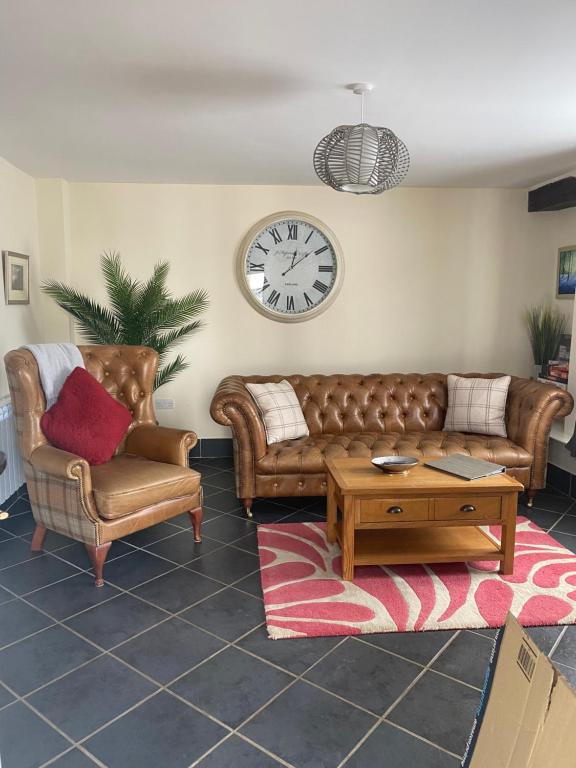 a living room with a couch and chairs and a clock at 2 Mews Cottages - Town Centre Location in Appleby