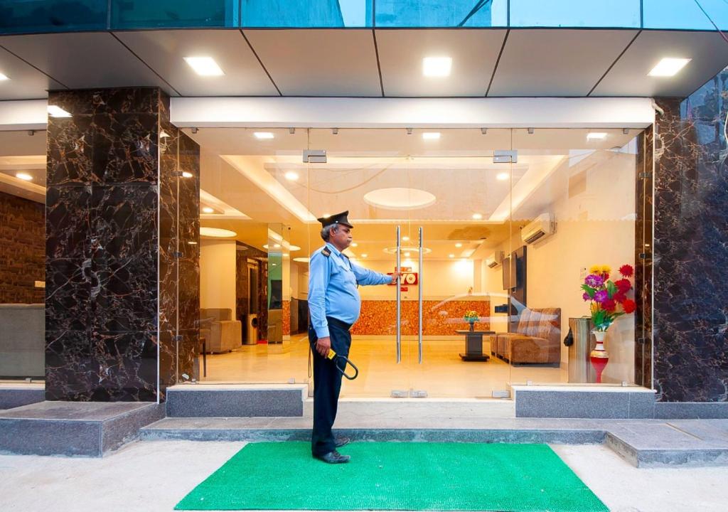 Hotel Bellwood Grand Near Delhi IGI Airport في نيودلهي: رجل في قبعة التخرج يقف على سجادة خضراء