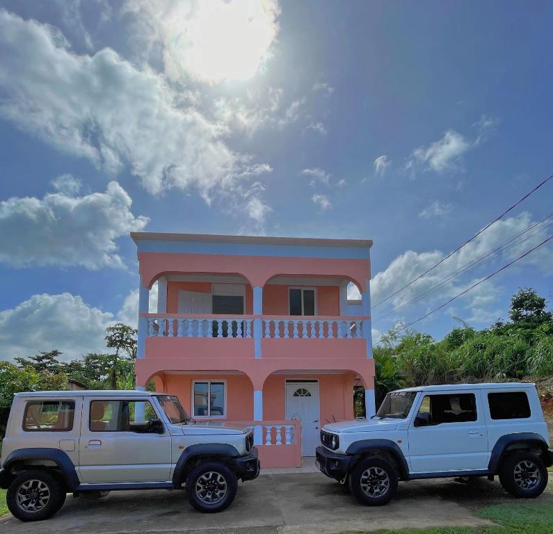 dwa jeepy zaparkowane przed różowym domem w obiekcie Happy-Nest (First floor) w mieście Marigot