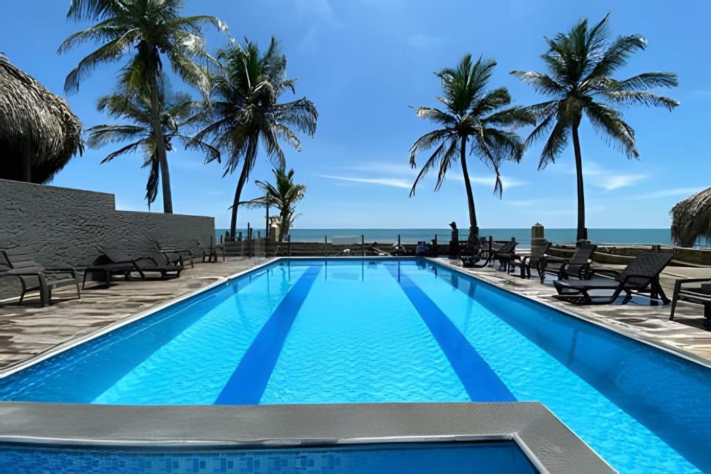 una piscina con palmeras y el océano en HERMOSOS APARTAMENTOS FRENTE AL MAR EN EL CONDOMINIO PALMAR DE LOS VIENTOS, en San Bernardo del Viento