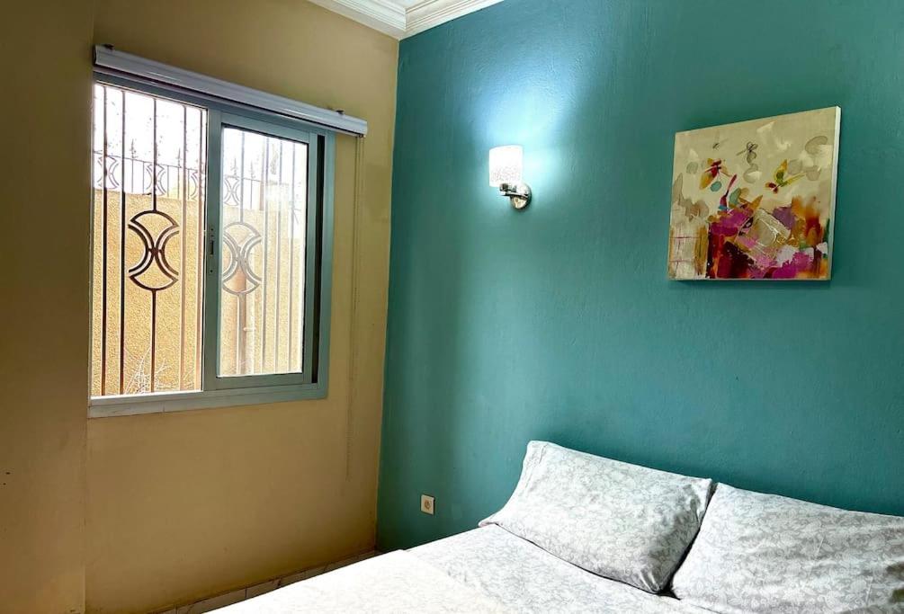 een slaapkamer met een blauwe muur, een bed en een raam bij Studio 1 Ch. Biteng Yaoundé in Yaoundé