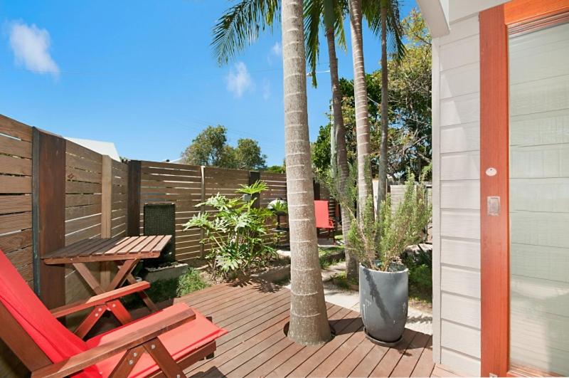 a deck with a wooden table and a bench and palm trees at Byron Bay Accom - Alkira 1/32 Alcorn St in Suffolk Park
