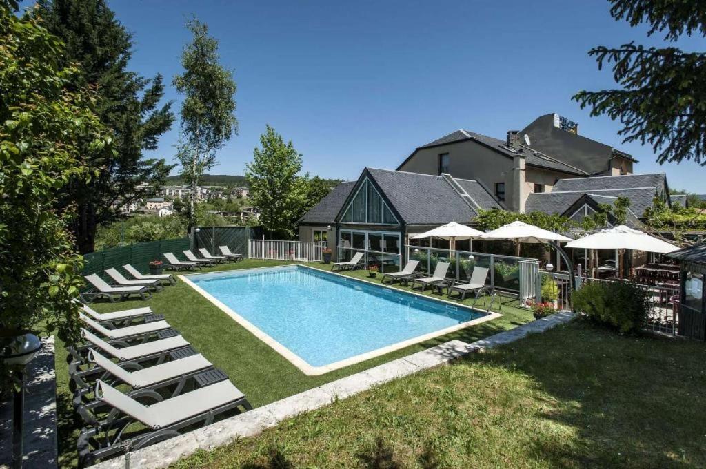 a swimming pool with lounge chairs and a house at Brit Hotel Confort Deltour Mende in Mende