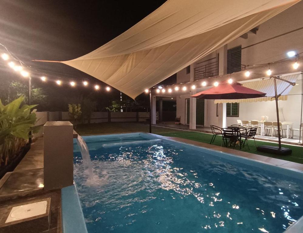 a swimming pool with a umbrella and a table and a house at AYRA HOMESTAY in Kuala Kangsar