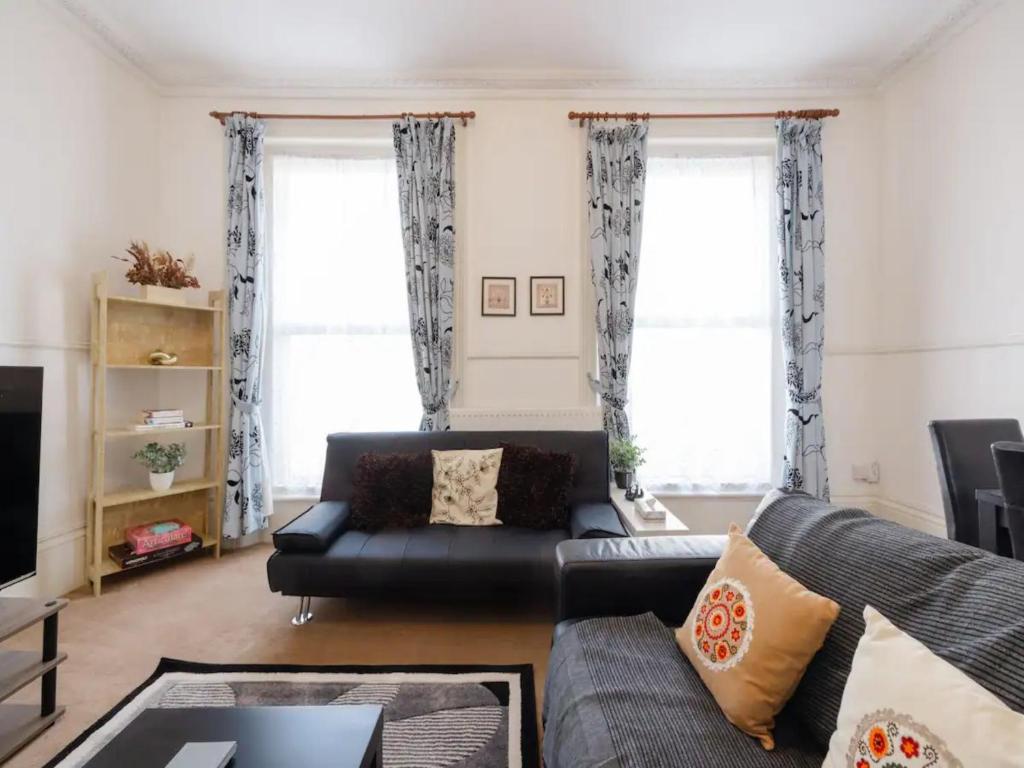 a living room with a black couch and two windows at Pass the Keys Spacious 3 Bed Flat Near Kings Cross and Camden in London
