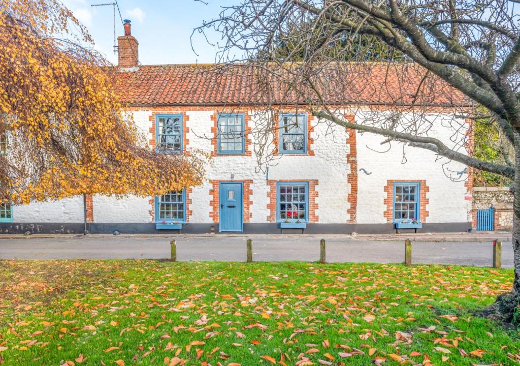 a white building with blue doors and a tree at Green Side Cottage in Thornham