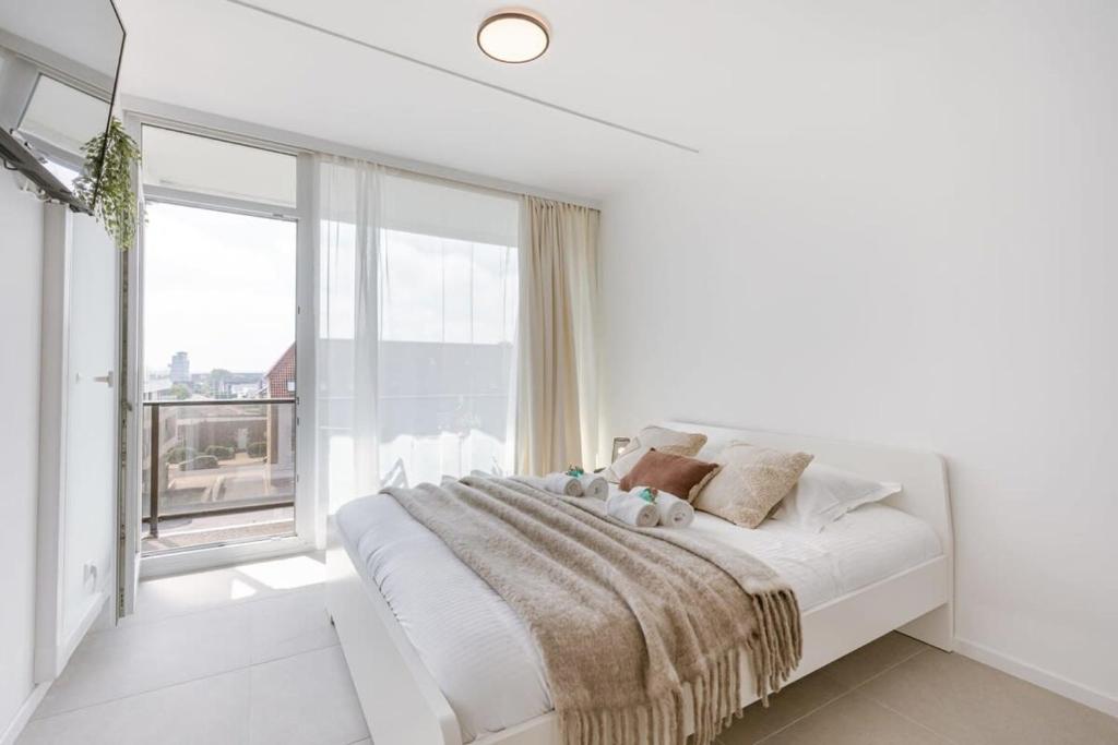 Dormitorio blanco con cama y ventana grande en Modern studio near the beach, en Ostende