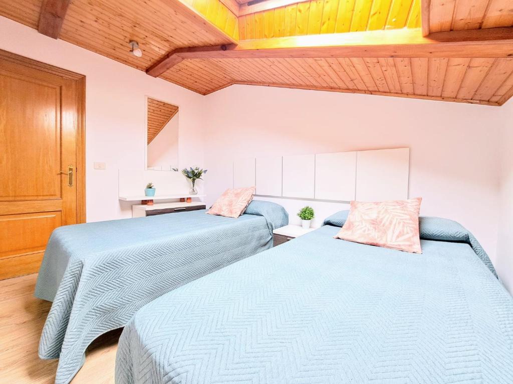 two blue beds in a room with wooden ceilings at Buen Camino - Arzúa Centro in Arzúa