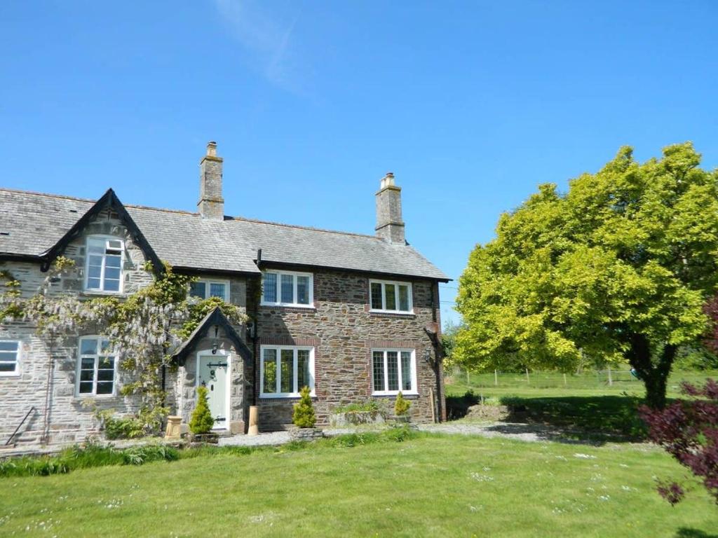 an old stone house with a tree in the yard at Victorian cottage overlooking the Plym Valley in Bickleigh