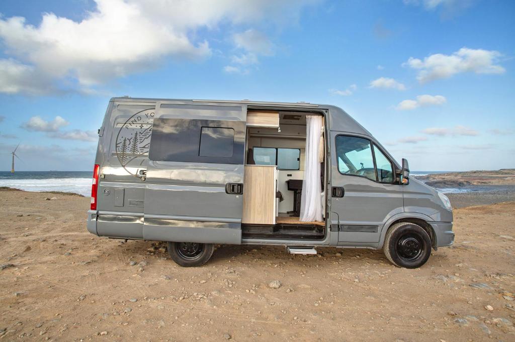 una furgoneta estacionada en la playa con la puerta abierta en Camper Van - Encuentra tu camino, en Marzagán