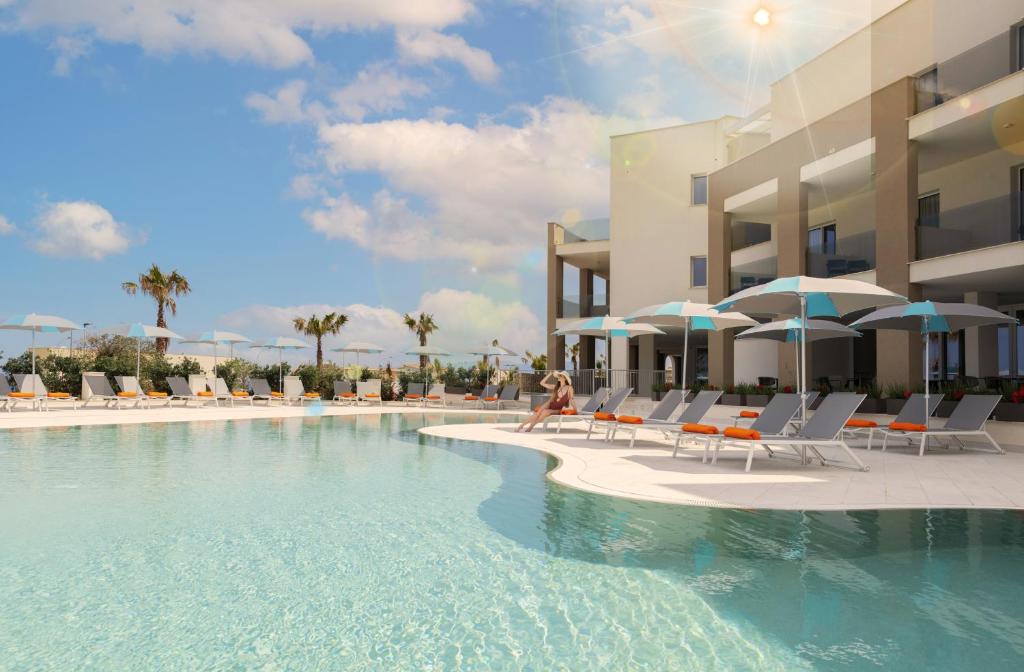 a pool with chairs and umbrellas next to a building at Resort La Battigia Beach & Spa in Alcamo Marina