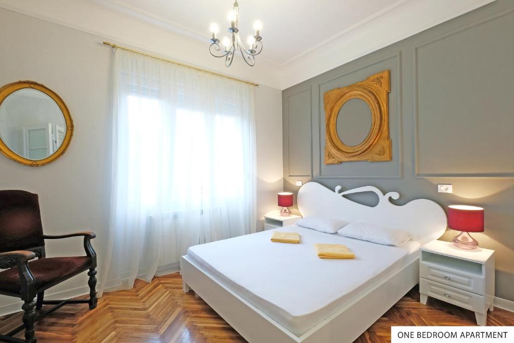 a bedroom with a white bed with a chair and a mirror at Downtown Belgrade Apartments in Belgrade
