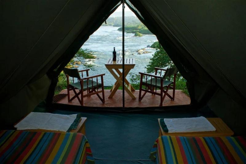 een tent met een tafel en stoelen en uitzicht op de oceaan bij Explorers River Camp in Jinja